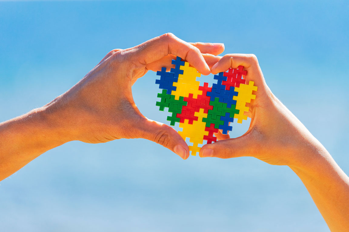 hands in the form of a heart holding up the autism logo in puzzle pieces
